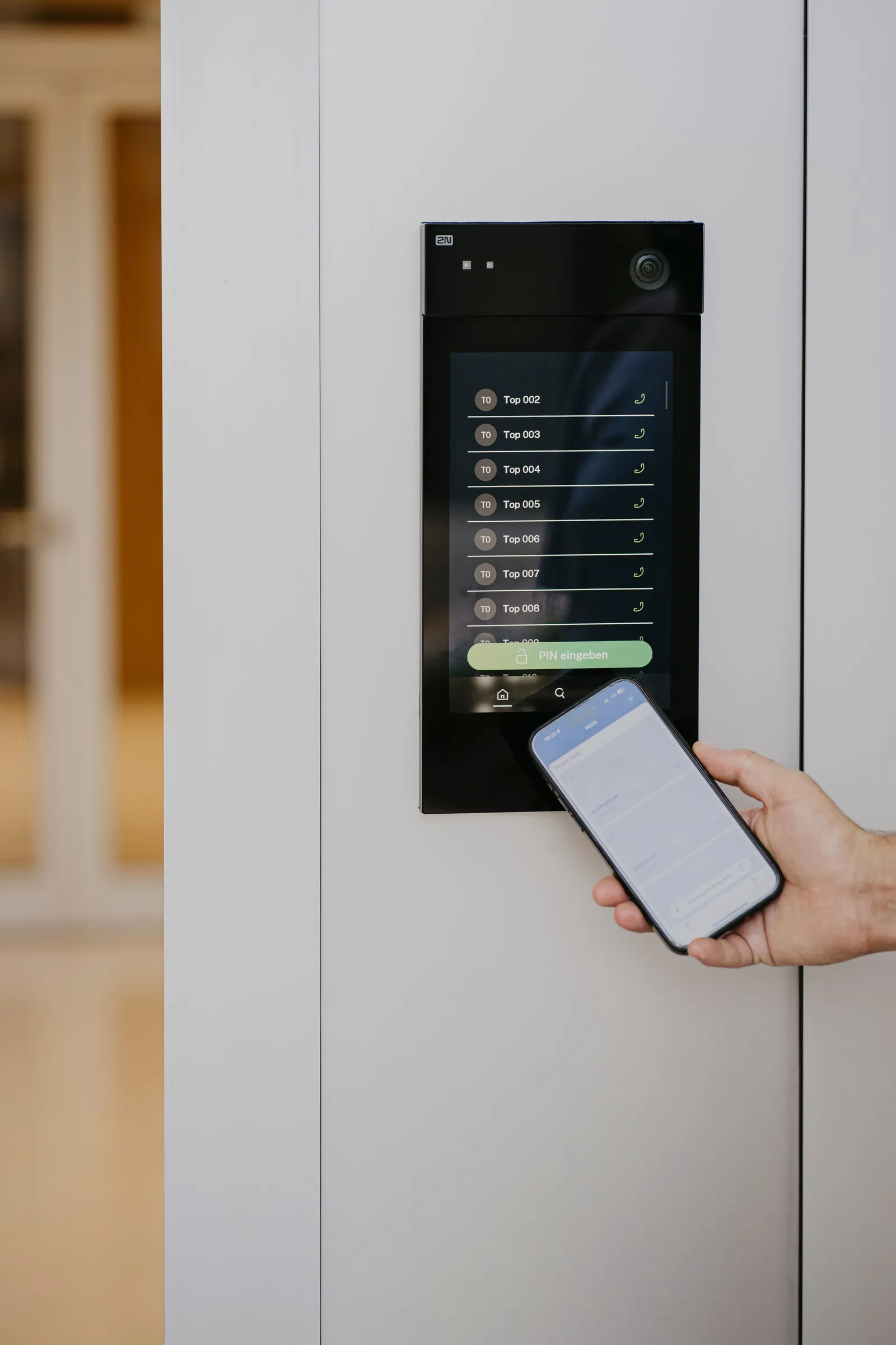 Portier vidéo 2N IP Style à écran tactile encastré près d’une porte, ouvert depuis un smartphone