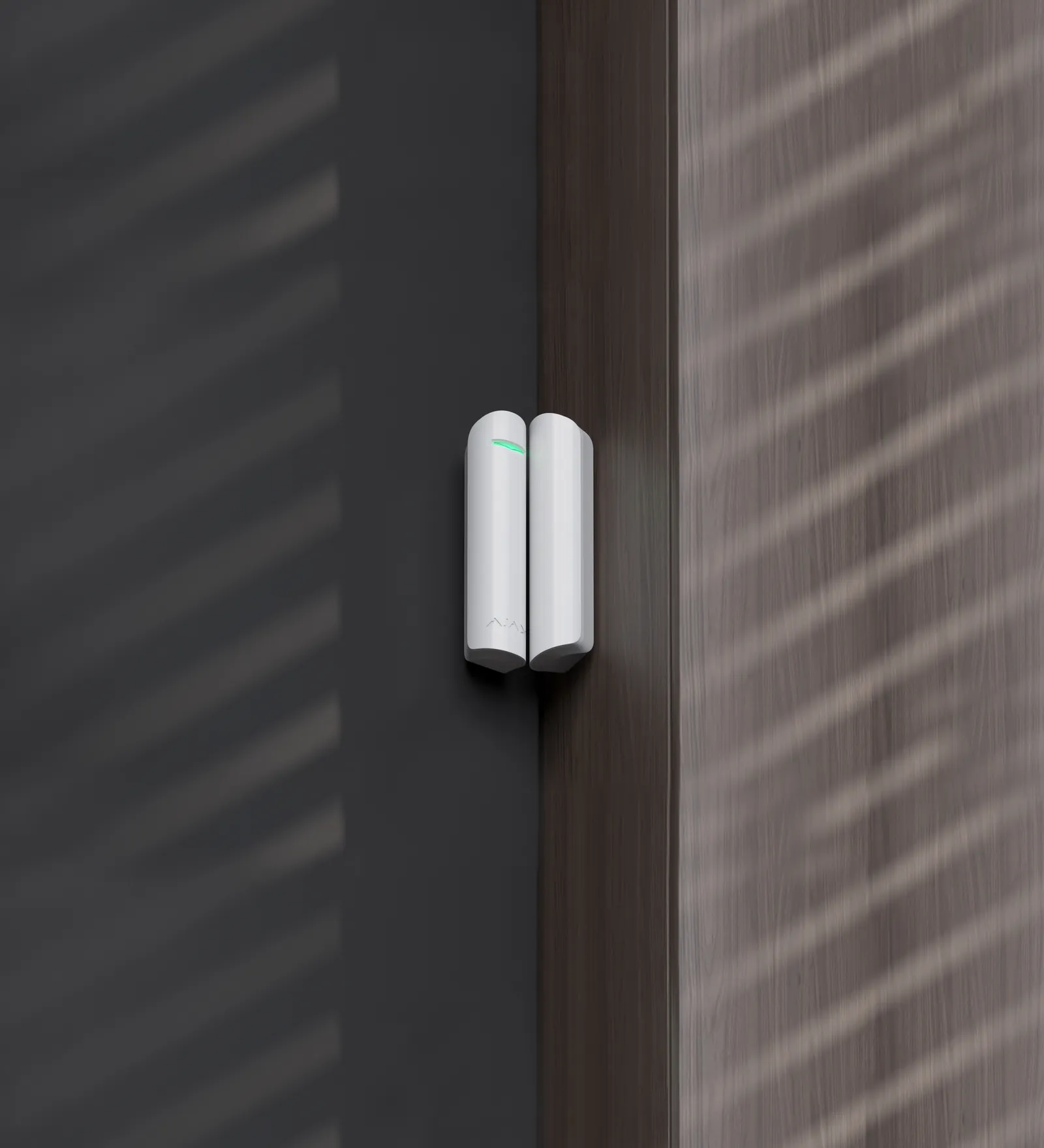 Contact d’ouverture Ajax DoorProtect blanc posé sur le chambranle d’une porte sombre