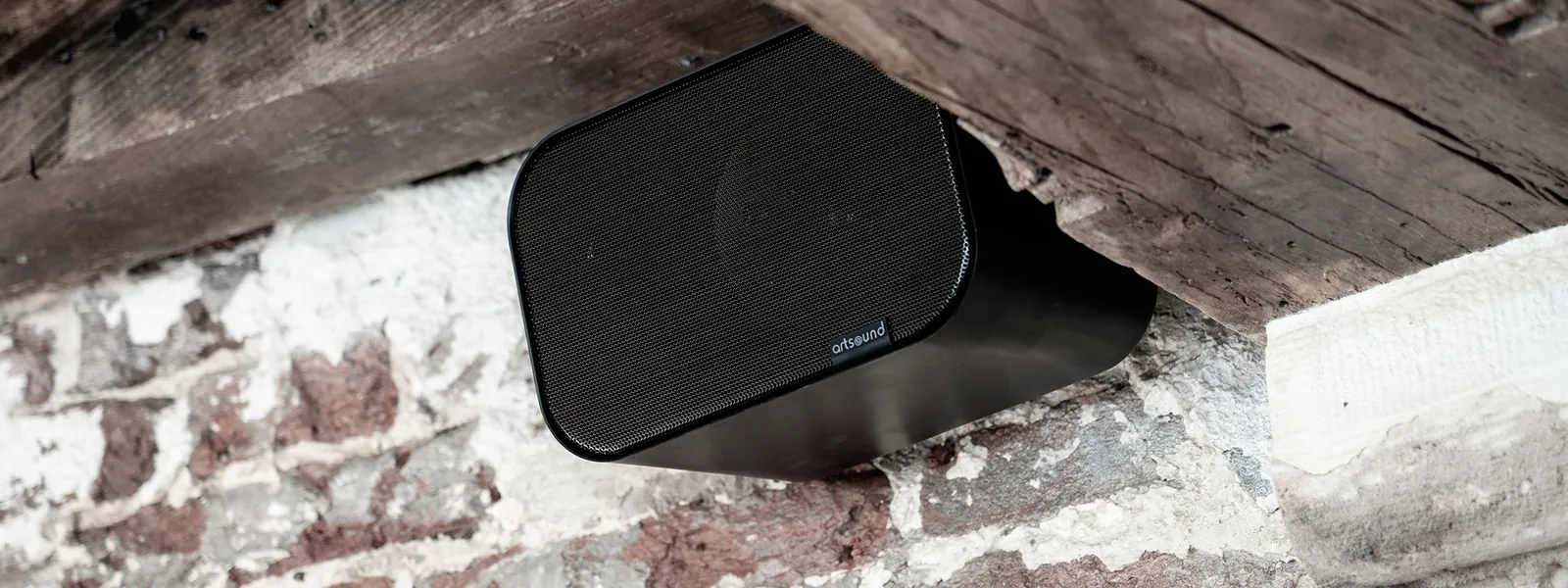 Enceinte murale ArtSound noire fixée sous une poutre en chêne ancien, mur de briques chaulées