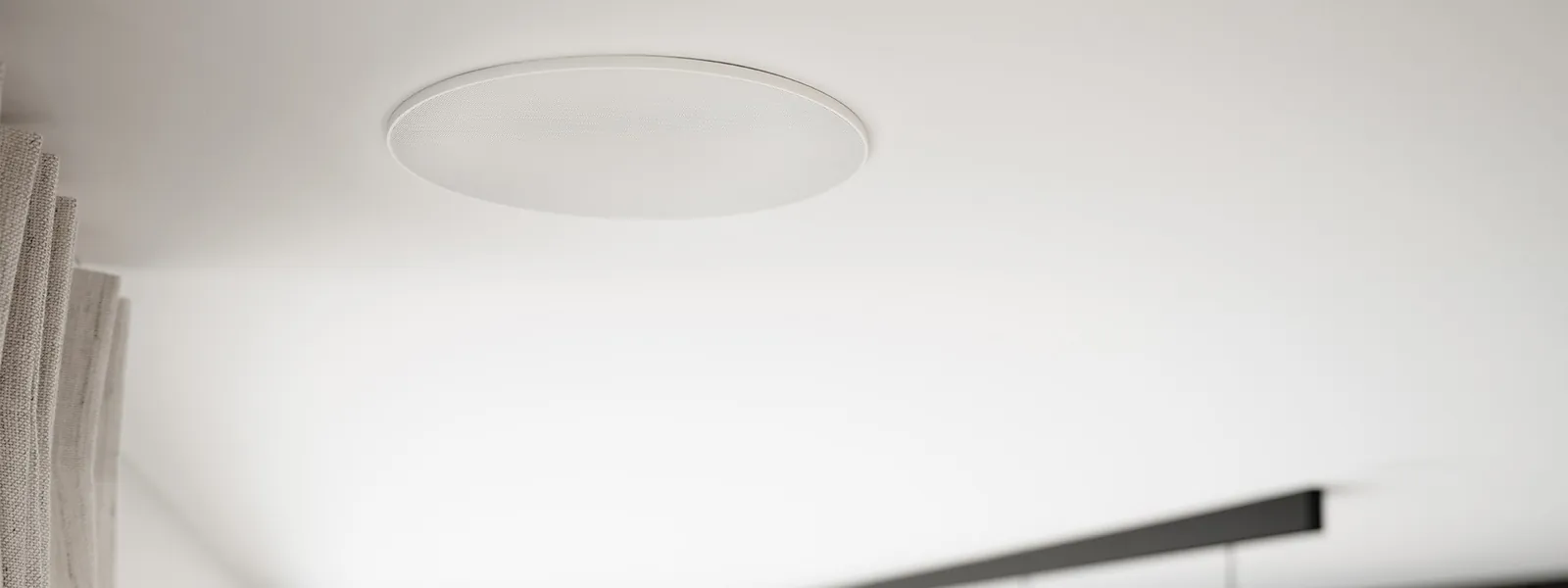 Enceinte ronde ArtSound encastrée à fleur dans un plafond blanc, rideau en lin
