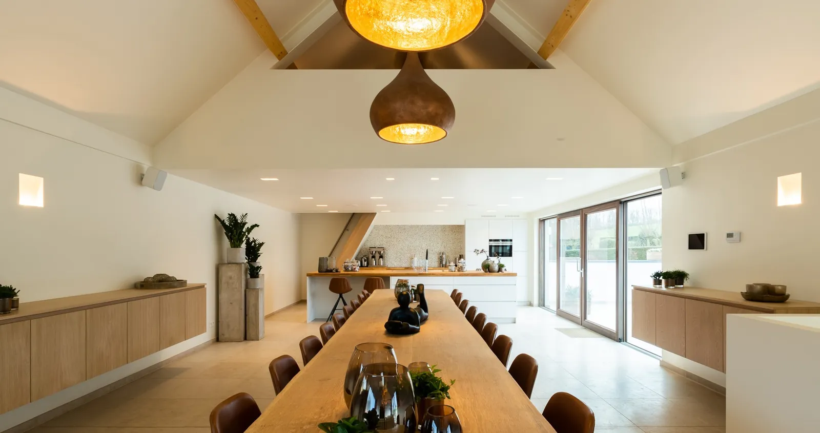 Grande salle à manger sous charpente, longue table en bois et enceintes murales ArtSound discrètes