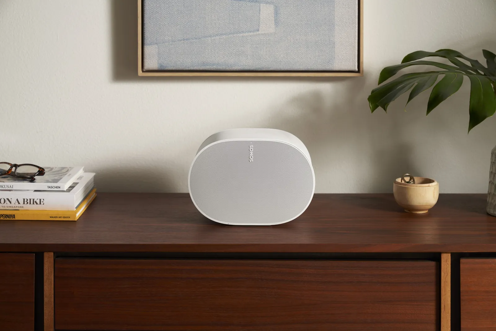 Enceinte Sonos Era 300 blanche sur un buffet en noyer, entre des livres et une plante