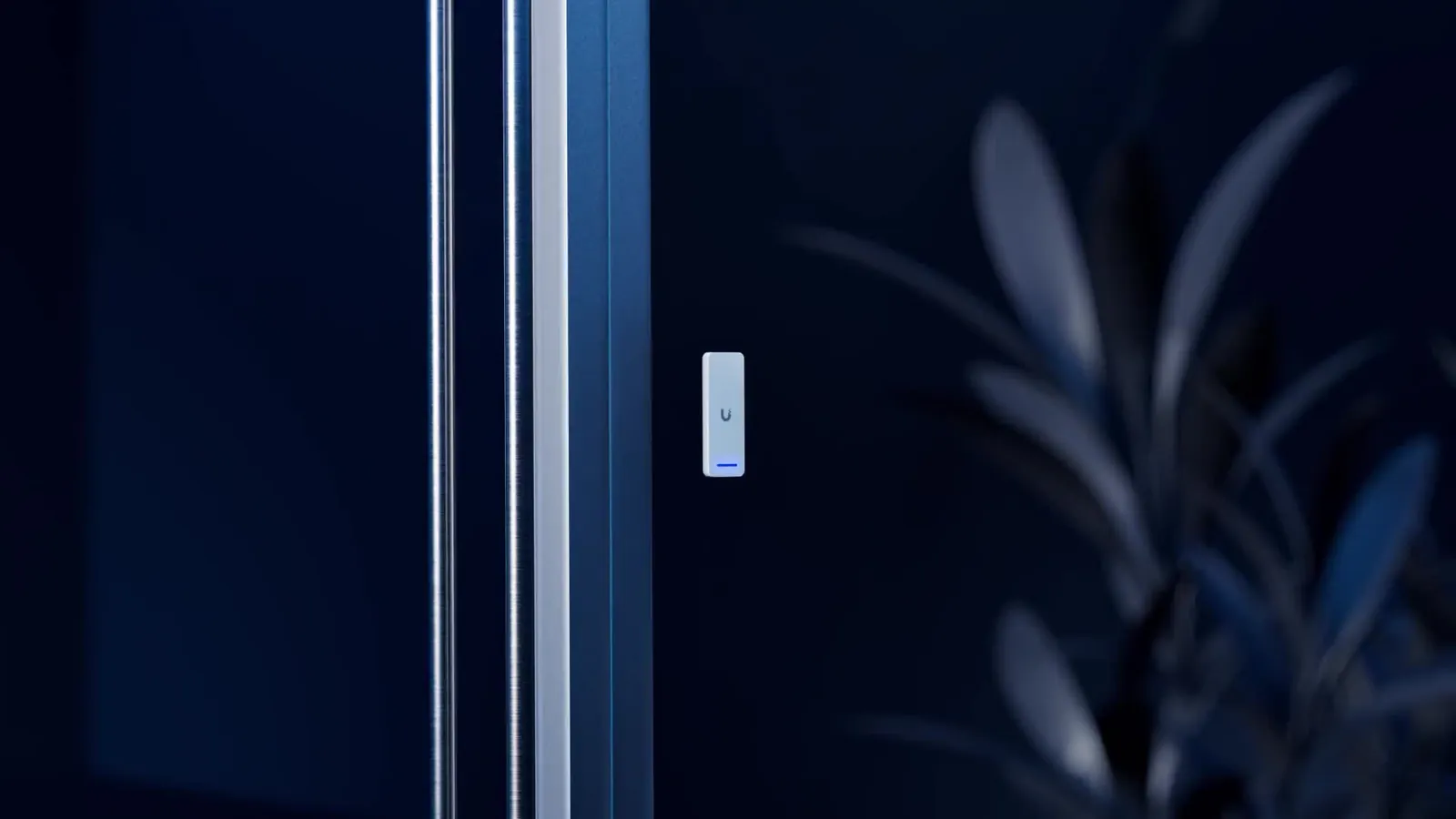 UniFi Access G3 Reader-badgelezer op het aluminium kozijn van een deur, bij nacht