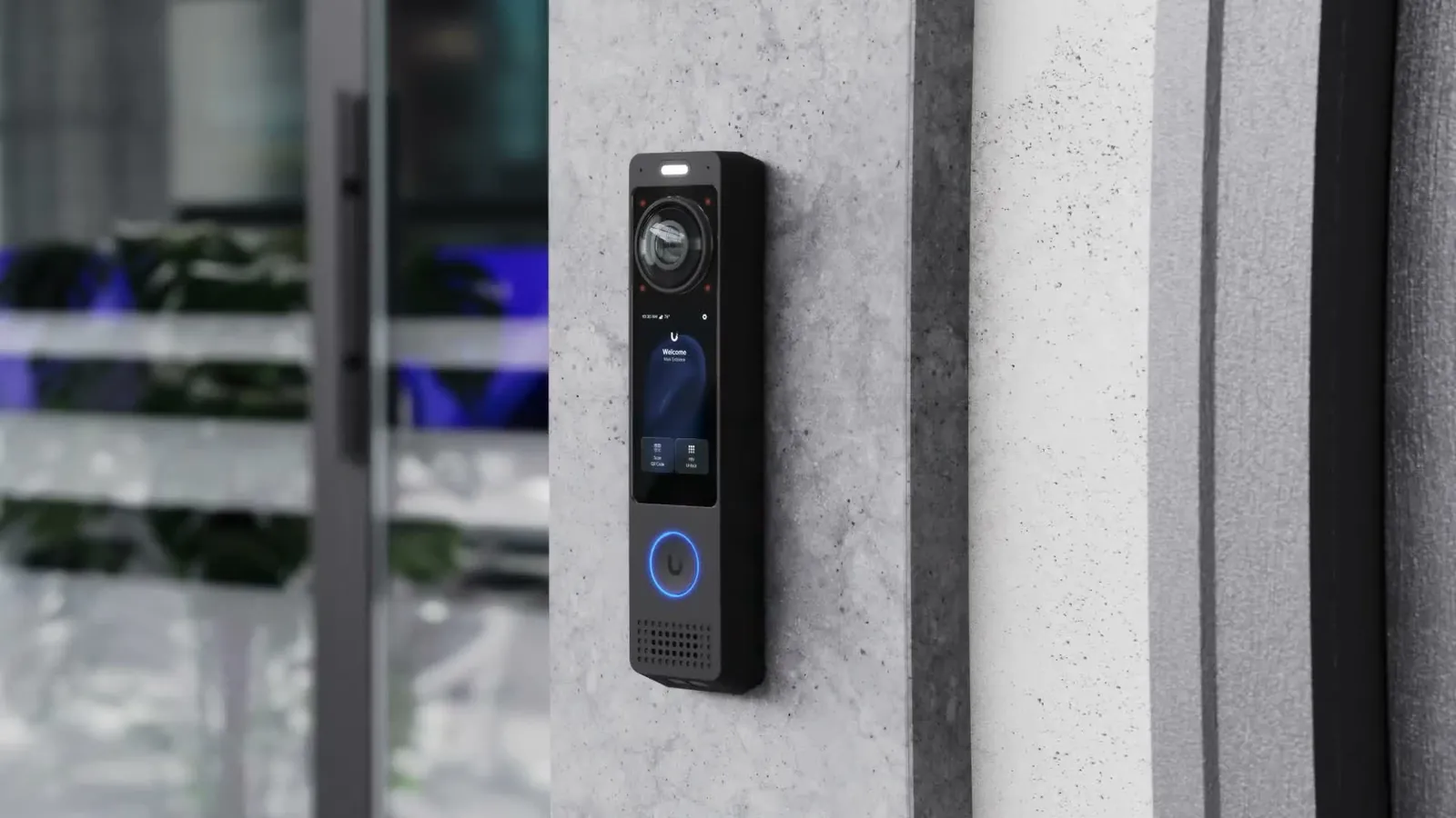 Platine d’entrée vidéo UniFi Access G6 Pro Entry sur un pilier en béton, porte vitrée en arrière-plan