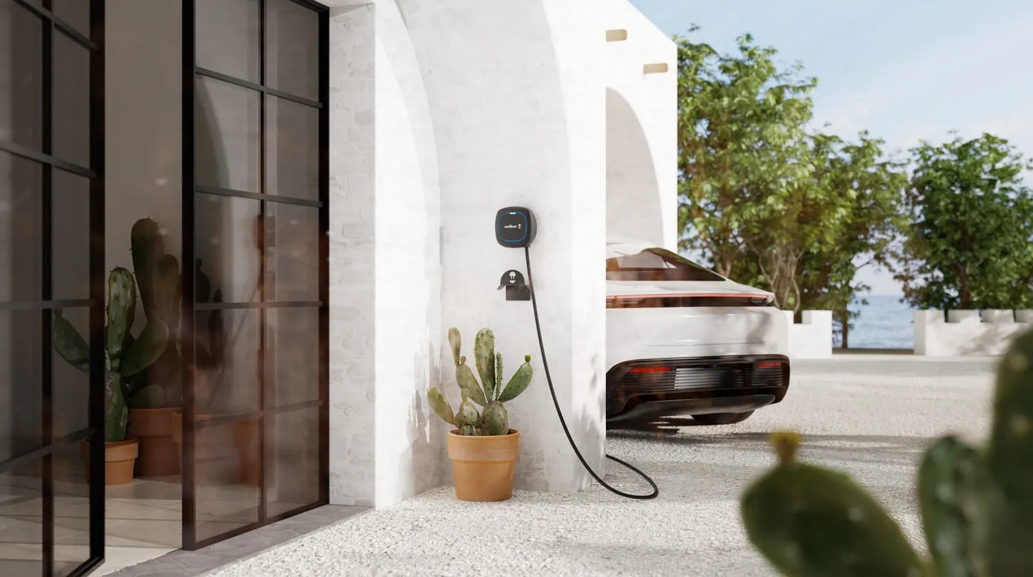 Black Wallbox Pulsar Max charger on the white façade of a villa, with an electric car charging